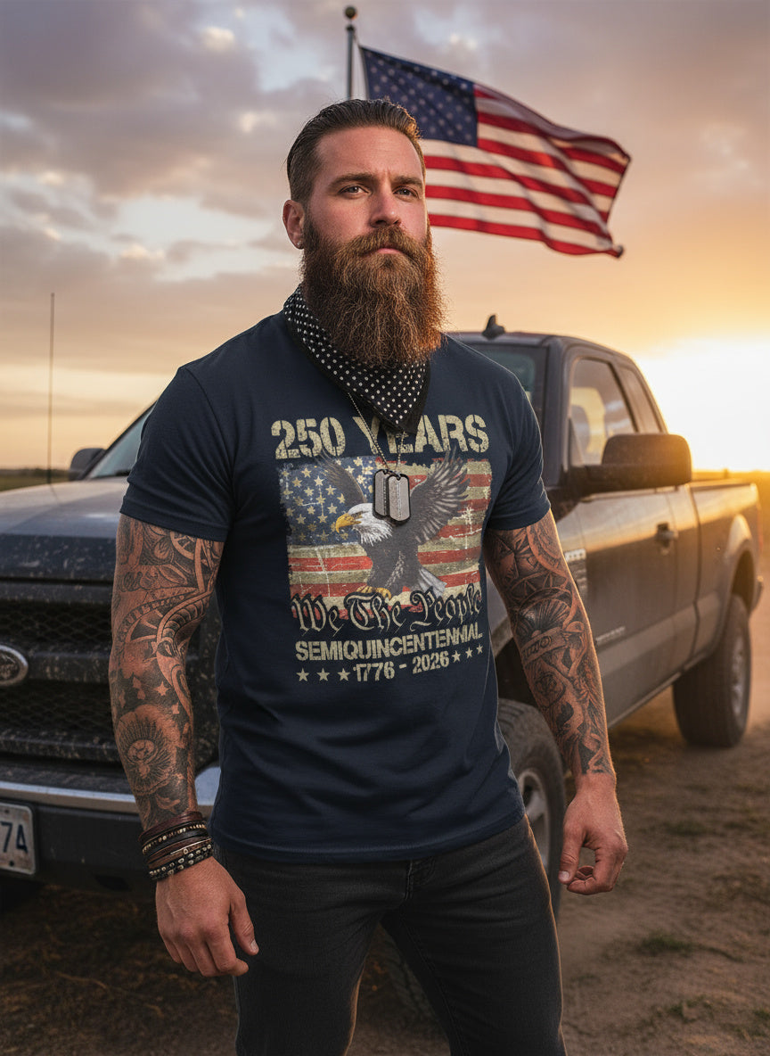 Man with tattoos wearing a blue t-shirt with an eagle design and text, standing in front of a truck with an American flag.